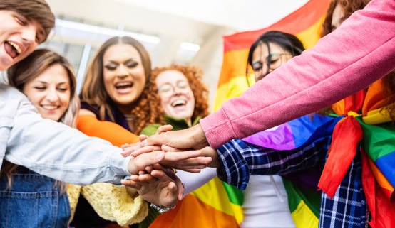A diverse group joining hands around a rainbow pride flag